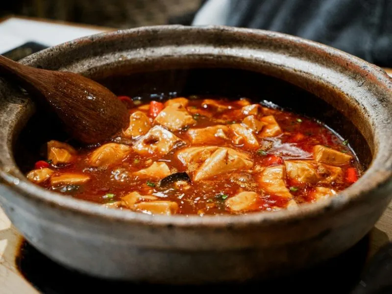 Spicy mapo tofu simmering inside rustic clay pot with wooden spoon at China Moon, a Chinese Restaurant in Twinsburg